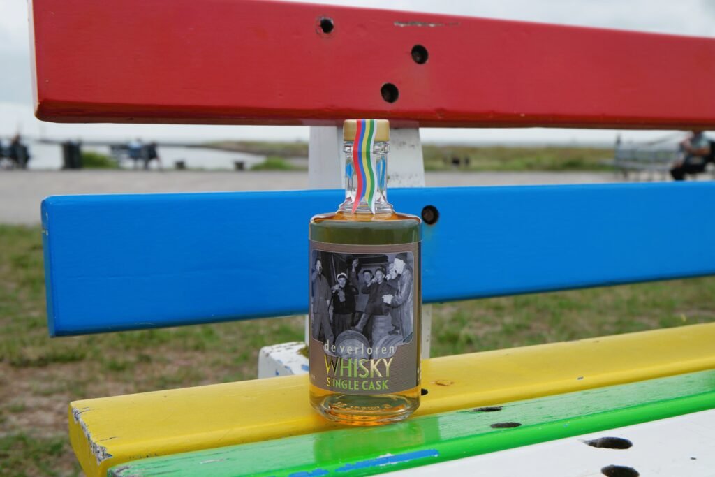 A bottle of De Verloren Whisky Single Cask sitting on a bench at Terschelling