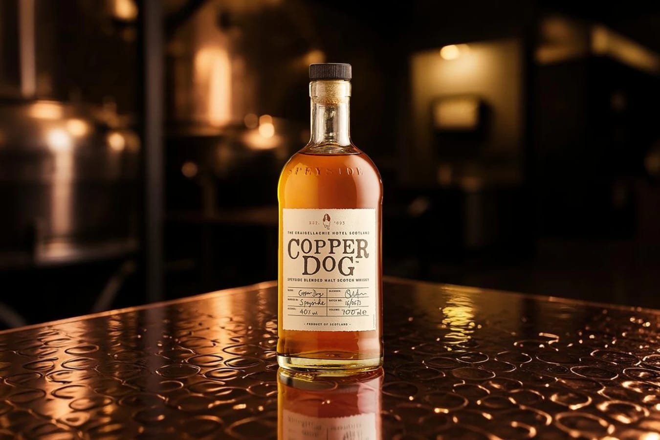Bottle of Copper Dog Speyside Blended Malt Scotch Whisky standing on a copper bar inside a distillery